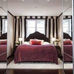 Elegantní postel u okna v místnosti se zrcadlovými skříňkami