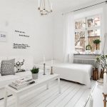 Vitt vardagsrum med vita möbler längs en vägg.