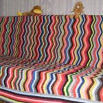 Plaid på en soffa från flera färgade vågiga remsor
