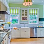 La luminosa e spaziosa cucina ha un muro di accento verde chiaro e tende verdi con strisce bianche.
