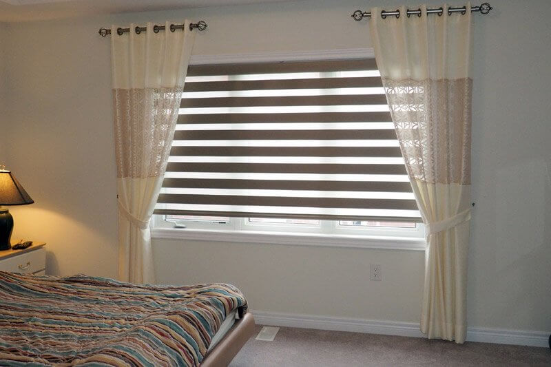 La combinaison de rideaux zébrés avec des rideaux droits sur la fenêtre de la chambre