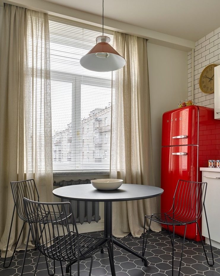 Punainen jääkaappi lähellä keittiön ikkunaa, jossa on kevyet verhot