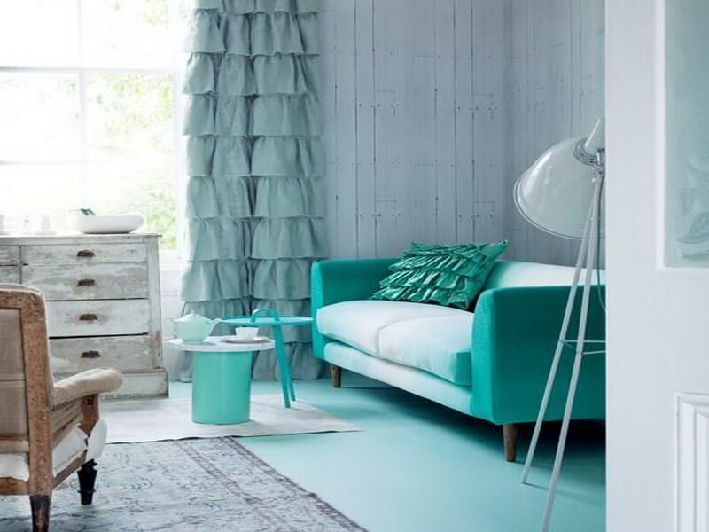 Turkis soffa bredvid mintfärgad gardin