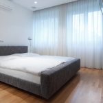 Grijs bed in de slaapkamer met witte gordijnen