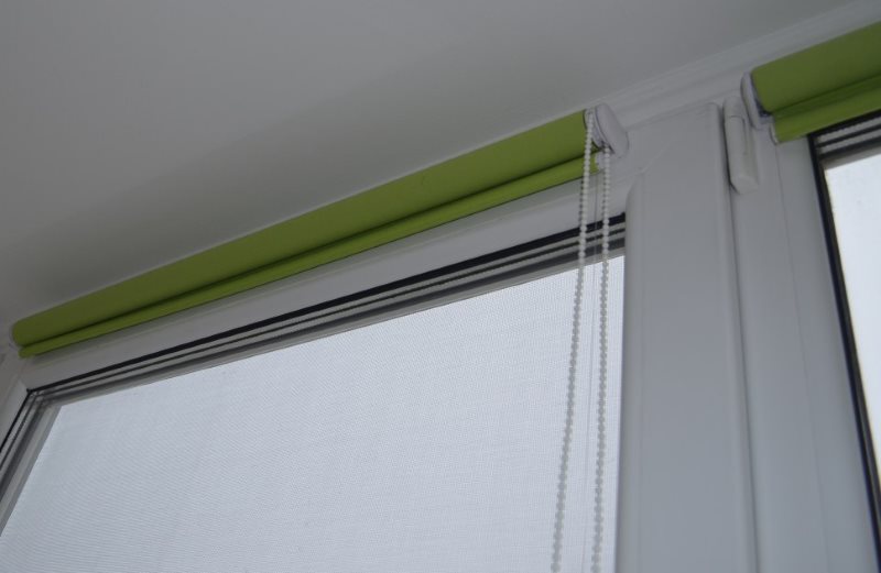 Rullade gardiner av grön färg på ett plastfönster